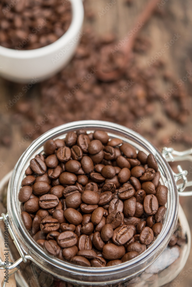 Full of Roasted coffee beans in a bottle and white cup of coffee on the old wood table background.
