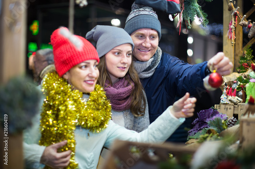 satisfied family couple with teen daughter choosing Christmas decoration