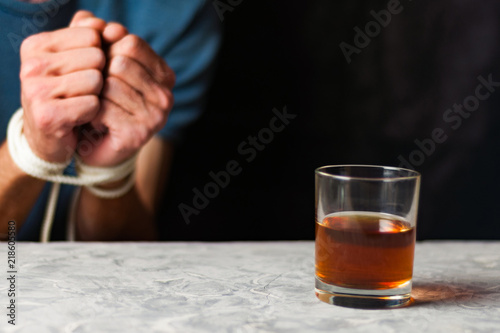 Transparent glass with alcohol on gray cement on background of man with tied hands