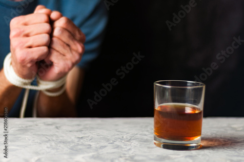 Fotografie Transparent glass with alcohol on gray cement on background of man with tied han