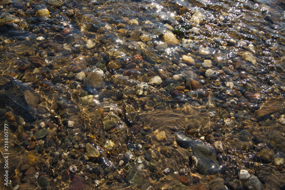 Various size and color of pebble and round stones under shallow clear flowing and streaming water in the canal and river 