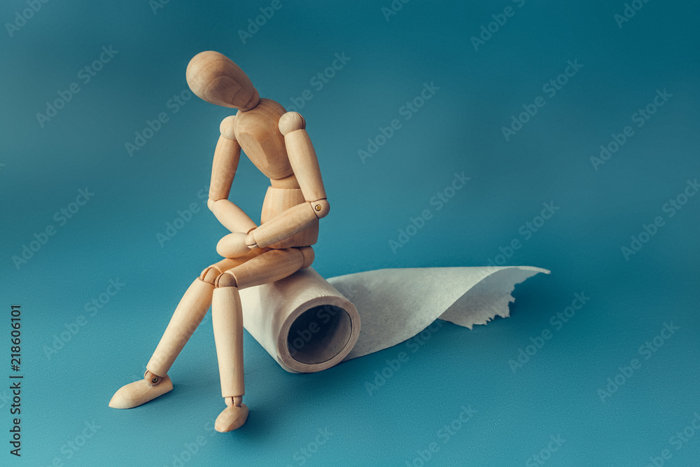 Wooden figure sit on a roll of toilet paper. Concept of the problem with digestion.