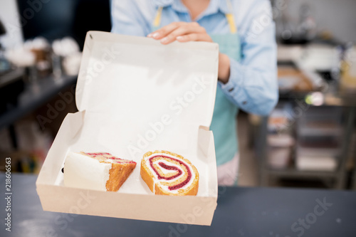 Close up of unrecognizable woman holding open box with delicious sweet roll over counter in small bakery, copy space
