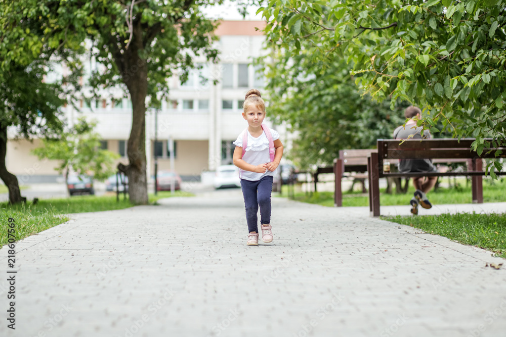 A little girl is walking with a backpack down the street. The concept of school, study, education, friendship, childhood A little girl is walking with a backpack down the street. The concept of school, study, education, friendship, childhood