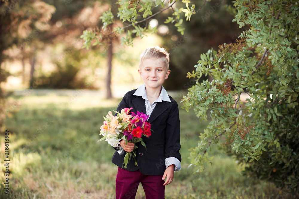 Fototapeta premium Smiling pupil boy holding flowers and wearing school uniform outdoors. Looking at camera. Back to school.
