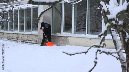 man clean cnow with shovel near house wall with big window. 4K photo