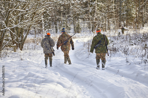 group of hunters in winter forest with carbines and shotgun photo