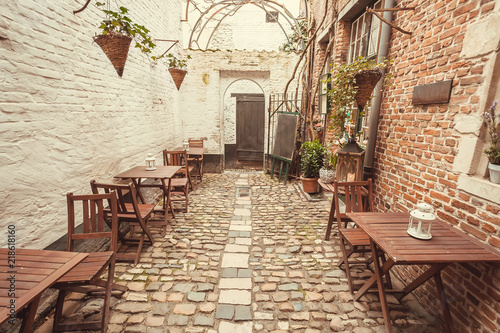 Empty space with wooden tables for hungry visitors of cozy outdoor restaurant in old style narrow street  with brick walls and cobbled stones