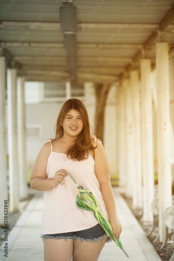 Asian pretty smiley face fat woman pose standing and hold umbrella on walkway. Asian pretty smiley face fat woman pose standing and hold umbrella on walkway.