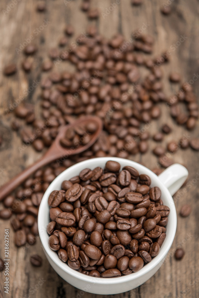 White coffee cup full of Roasted coffee beans on the old wood table background. (View from top)