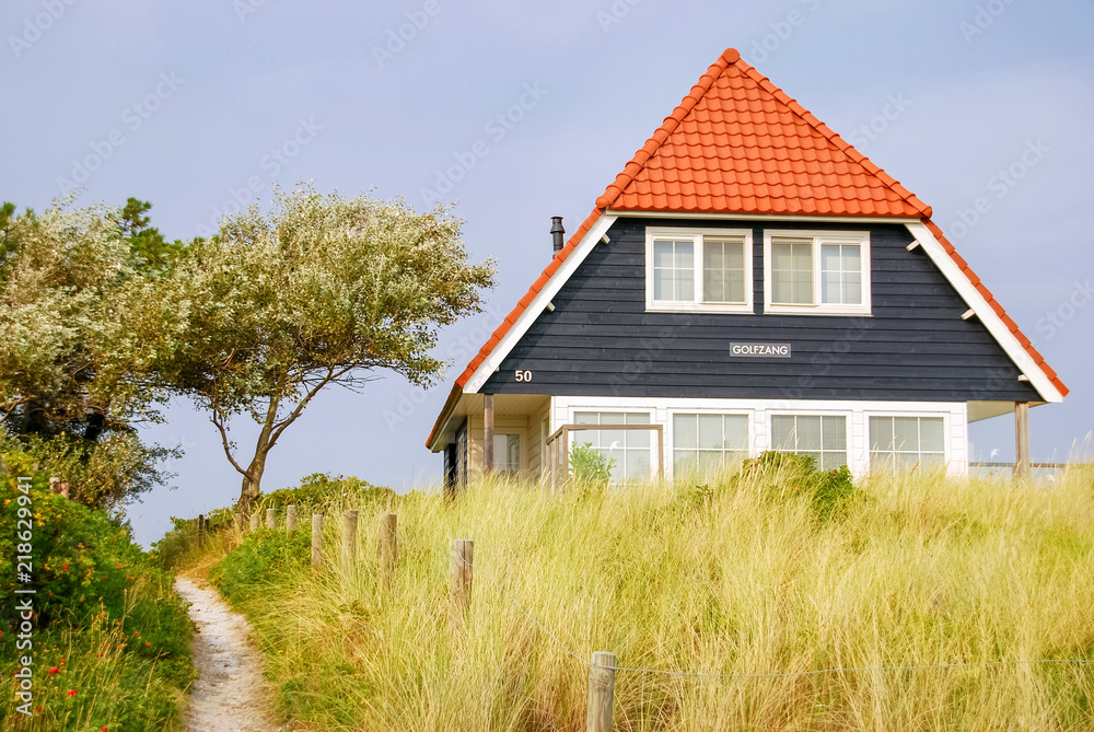Obraz premium A blue house and the Dutch flag on the Frisian Island of Vlieland, The Netherlands. The Frisian Islands, also known as the Wadden Islands or Wadden Sea Islands