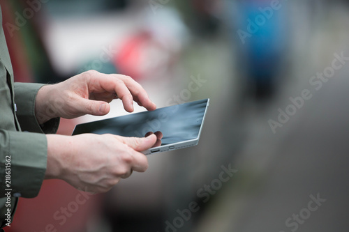 Businessman holding a smart tablet, mobile cell, stuck in traffic daytime. Man in shirt using tablet, cars in the background.