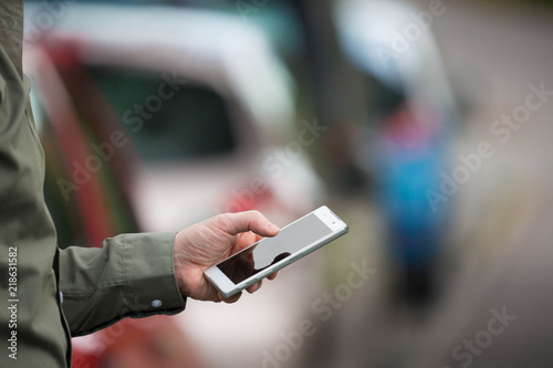 Businessman holding a smartphone, mobile cell, stuck in traffic daytime. Man in shirt texting, cars in the background.