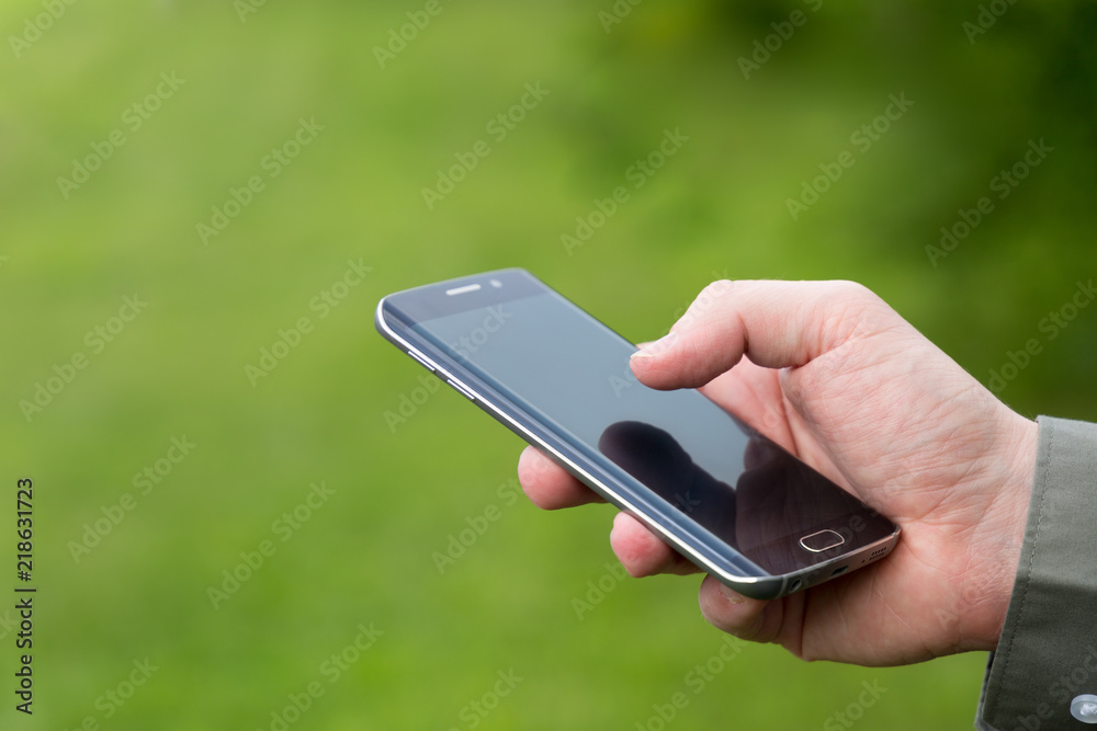 Businessman holding a smart phone, on a green summer day. place for your text