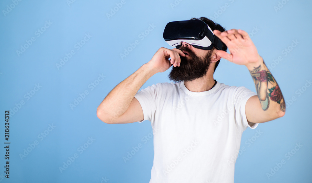 Man with beard in VR glasses, light blue background. Hipster on busy face exploring virtual reality with gadget. Interactive surface concept. Guy with head mounted display interact in virtual reality Man with beard in VR glasses, light blue background. Hipster on busy face exploring virtual reality with gadget. Interactive surface concept. Guy with head mounted display interact in virtual reality