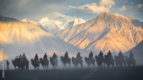 Caravan of people riding on camels in dusty Nubra valley photo