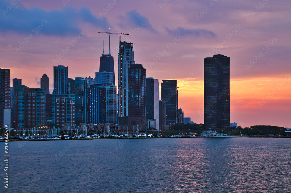 Obraz premium Colorful evening sunset over Chicago skyline with buildings of old, new and current construction, all of which is reflected onto Lake Michigan.