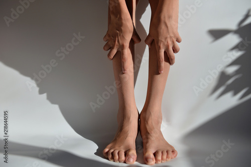 Hands and feet of a young man on a white background with a shadow. Hands clasp their legs