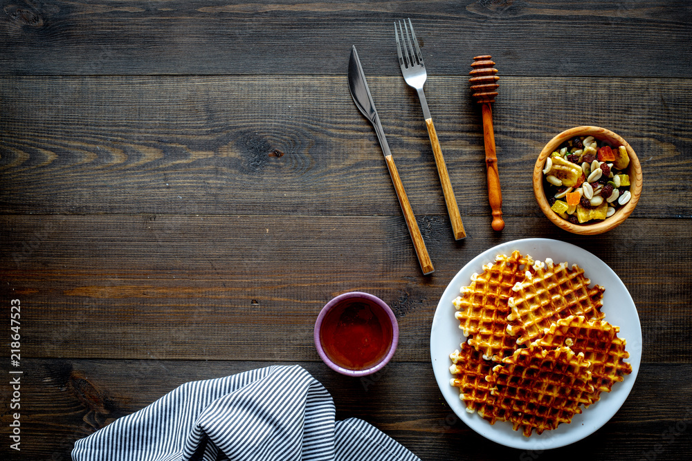 Fototapeta premium Traditional belgian waffles with dried fruit, nuts and caramel on dark wooden background flat lay copy space