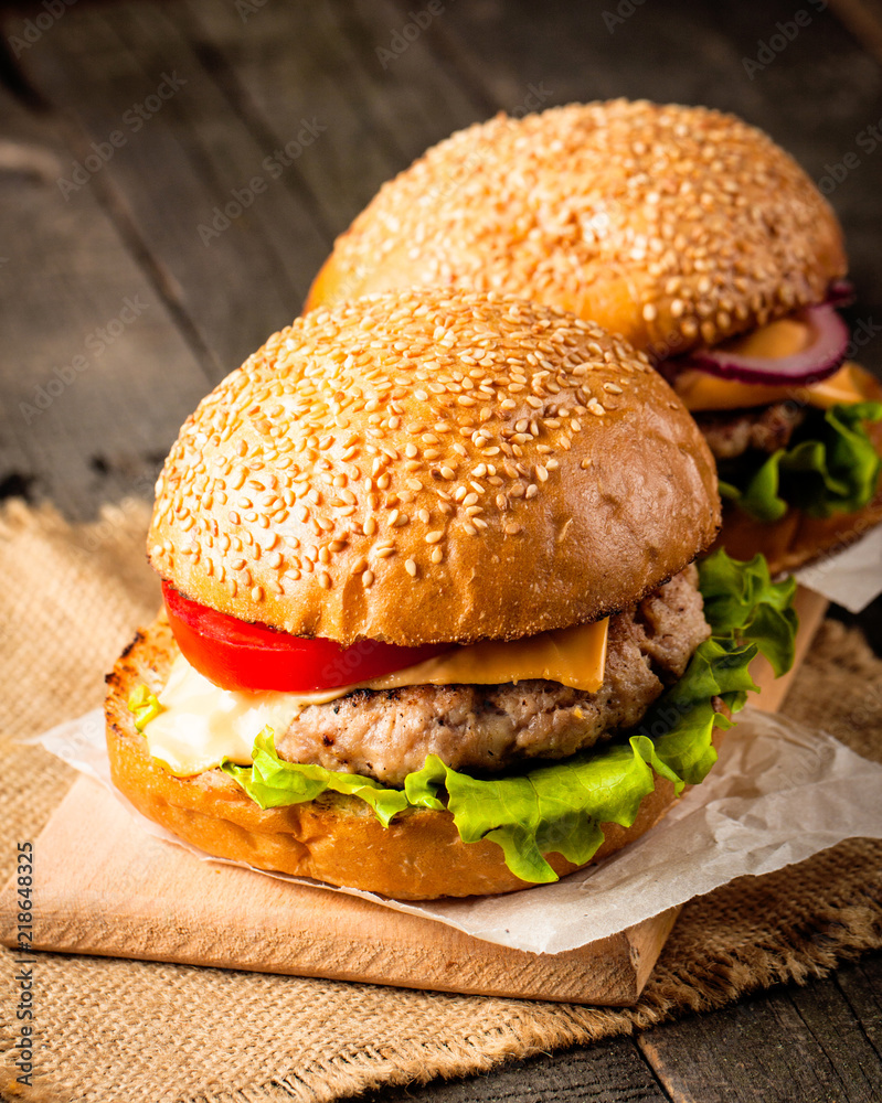 Close-up photo of home made hamburger with beer made of beef, onion, tomato, lettuce, cheese and spices. Fresh burger closeup on wooden rustic table with potato fries and chips. Close-up photo of home made hamburger with beer made of beef, onion, tomato, lettuce, cheese and spices. Fresh burger closeup on wooden rustic table with potato fries and chips.
