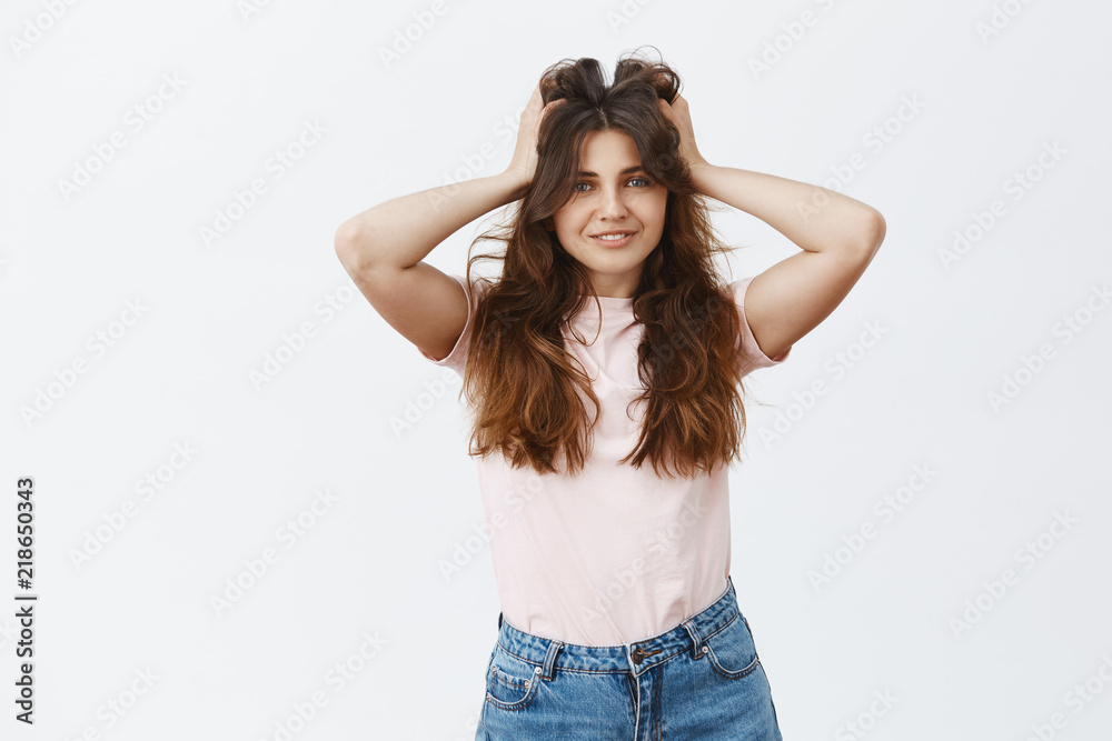 Indoor shot of happy and carefree woman feeling satisfied after vising hairdresser making incredible hair mask touching fluffy and beautiful hairstyle smiling broadly over gray background Indoor shot of happy and carefree woman feeling satisfied after vising hairdresser making incredible hair mask touching fluffy and beautiful hairstyle smiling broadly over gray background