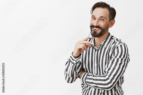 Nice joke mate. Portrait of joyful handsome adult uncle in striped shirt, biting rim of glasses and smiling happily at camera, being entertained and amused, having fun on business trip, talking © Cookie Studio