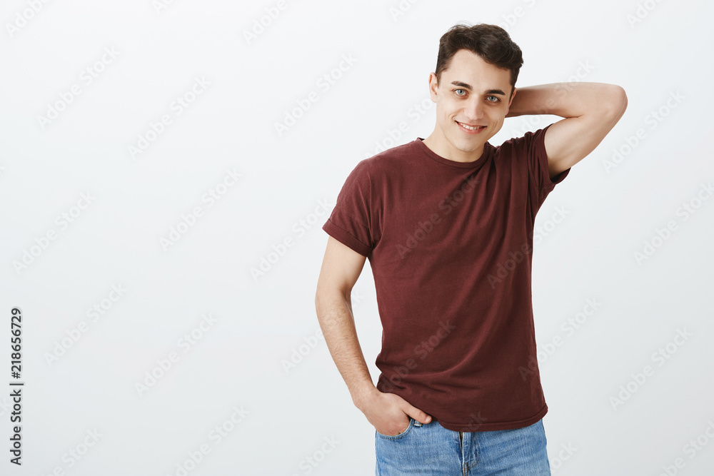 Studio shot of good-looking confident young man in red t-shirt, touching back of head and smiling playfully while flirting with woman in bar, asking number over gray background Studio shot of good-looking confident young man in red t-shirt, touching back of head and smiling playfully while flirting with woman in bar, asking number over gray background