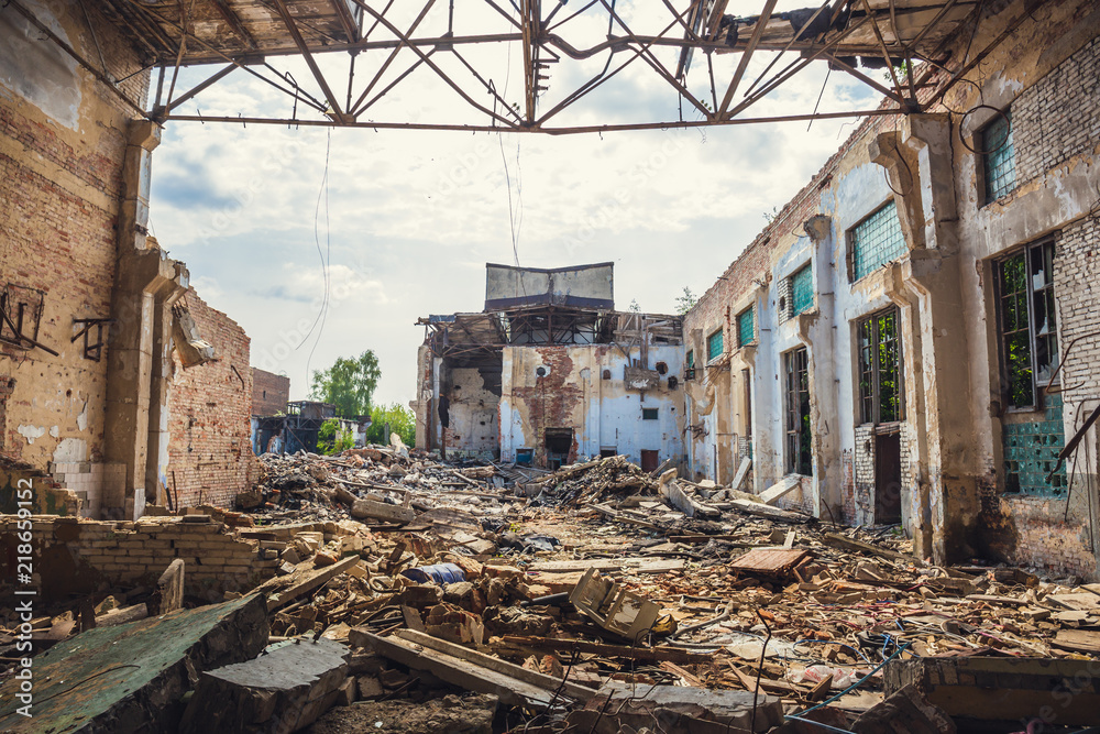 Fototapeta premium Ruined abandoned industrial building with large pills of concrete garbage, aftermath of natural disaster, hurricane, earthquake or war