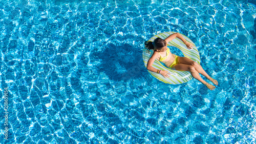 Aerial top view of little girl in swimming pool from above, kid swims on inflatable ring donut , child has fun in blue water on family vacation resort 