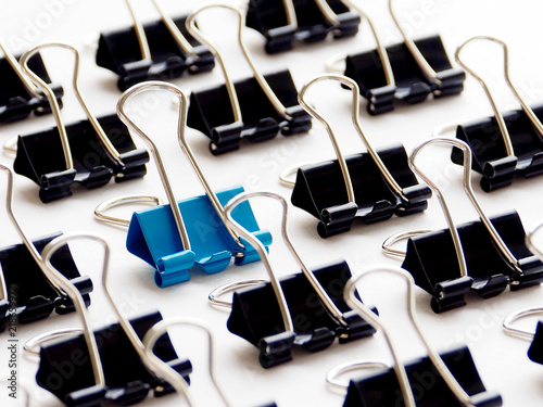 Closeup blue paper clip among black paper clips on white background, stand out of the crowd, uniqueness and outstanding concept 