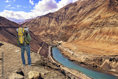 Tourist male backpacker enjoy an aerial view of Zanskar valley Ladakh with confluence point of Zanskar with river Indus. photo