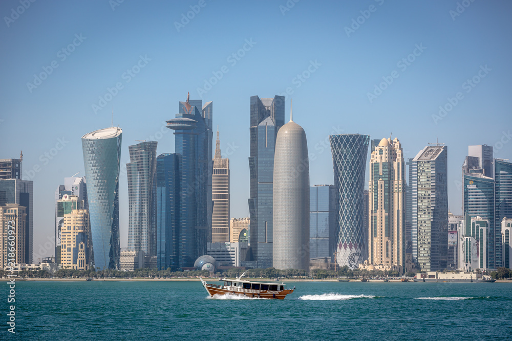 The skyline of Doha with a traditional boat in the foreground in Qatar, on a blue sky day, winter time, seen from the MIA Park