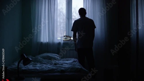Alone man silhouette staring at the window closed with curtains in bedroom. Man stands at window alone