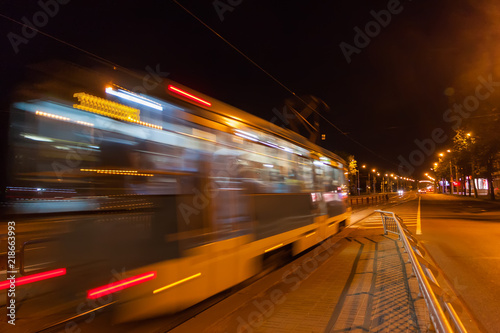 The motion of a blurred tram down the street in the evening.