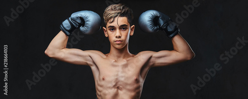 Handsome shirtless young boxer wearing gloves showing muscles. Isolated on the dark background.