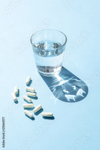 Water in glass Cup and white long capsules on a blue surface