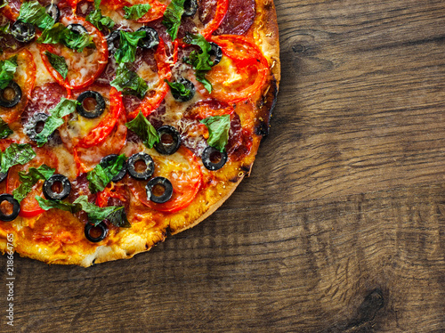 Pizza with Mozzarella cheese, salami, pepper, pepperoni, Tomatoes, olives, Spices and Fresh Basil. Italian pizza on wooden background. with copy space. top view