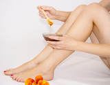 A girl is holding a bowl with a wooden spoon in her hands near her feet. With liquid sugar, for epilation. With liquid honey.