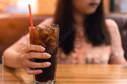 Young woman holding a glass of soft drink cola carbonated with ice on wooden table.
