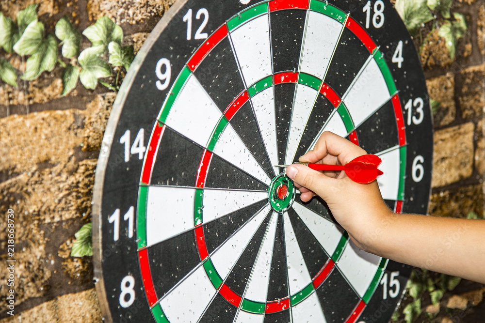 A man plays darts and holds the dart with his hand to hit the target on the target. A man plays darts and holds the dart with his hand to hit the target on the target.