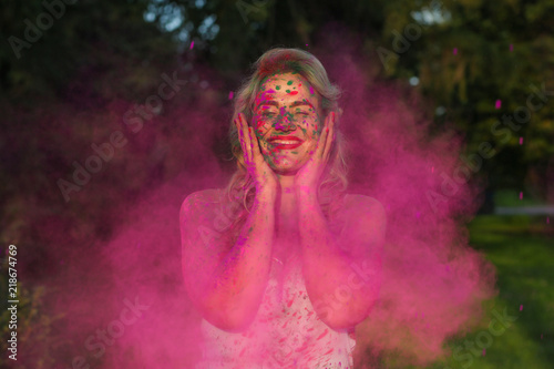Fototapeta Naklejka Na Ścianę i Meble -  Joyful caucasian girl with curly hair standing n a cloud of pink dry paint, celebrating Holi festival