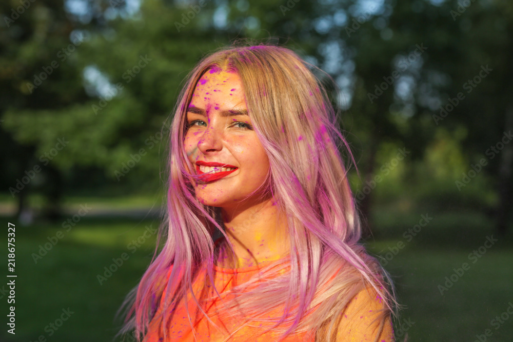 Expressive blonde girl with long hair covered purple dry paint celebrating Holi festival