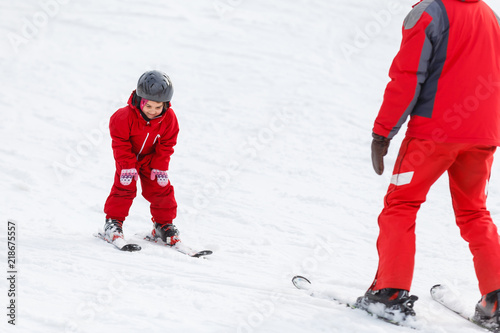 Professional ski instructor is teaching a child to ski on a sunny day on a mountain slope resort with sun and snow. Family and children active vacation.