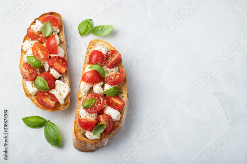 Bruschetta with tomatoes, mozzarella cheese and basil on a light background. Traditional italian appetizer or snack, antipasto. Top view with copy space. Flat lay