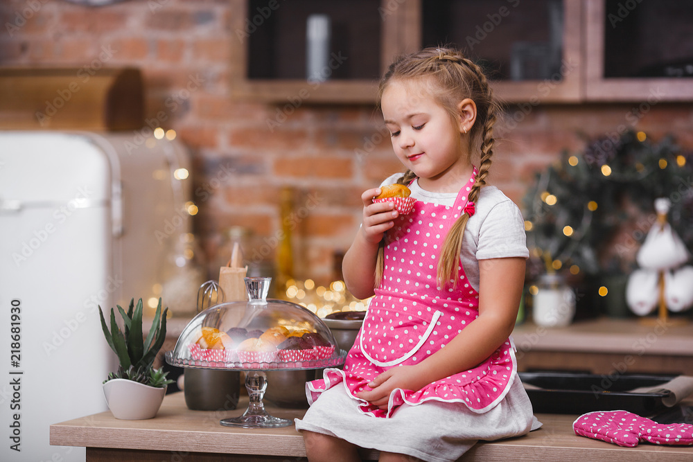 Fototapeta premium Little cute girl in the kitchen eating cupcakes