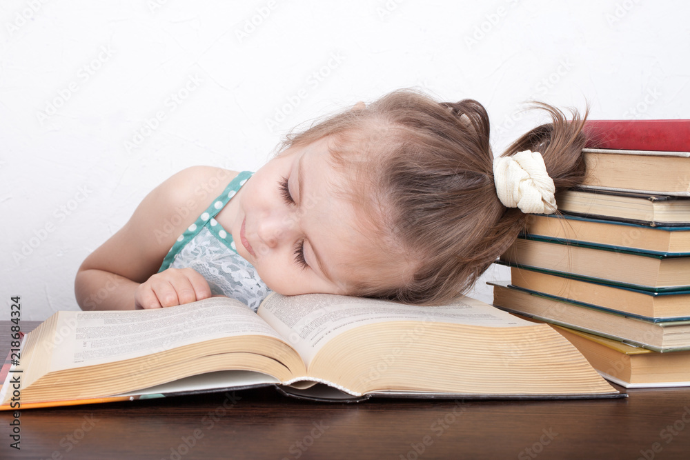 A little girl in glasses fell asleep behind textbooks A little girl in glasses fell asleep behind textbooks