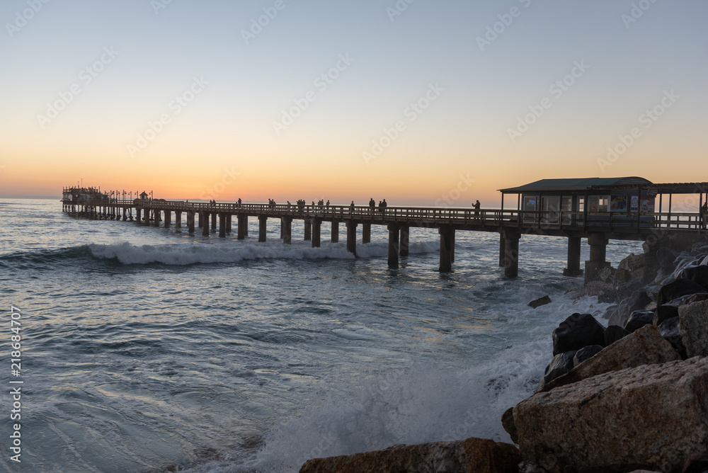 Pier at sunset with waves crushing against rocks at the coast, Swakopmund, Namibia