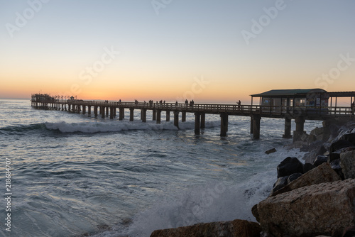 Pier at sunset with waves crushing against rocks at the coast  Swakopmund  Namibia