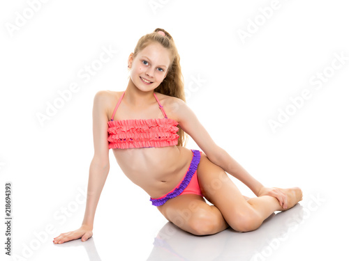 Beautiful little girl in a bathing suit is sitting on the floor.