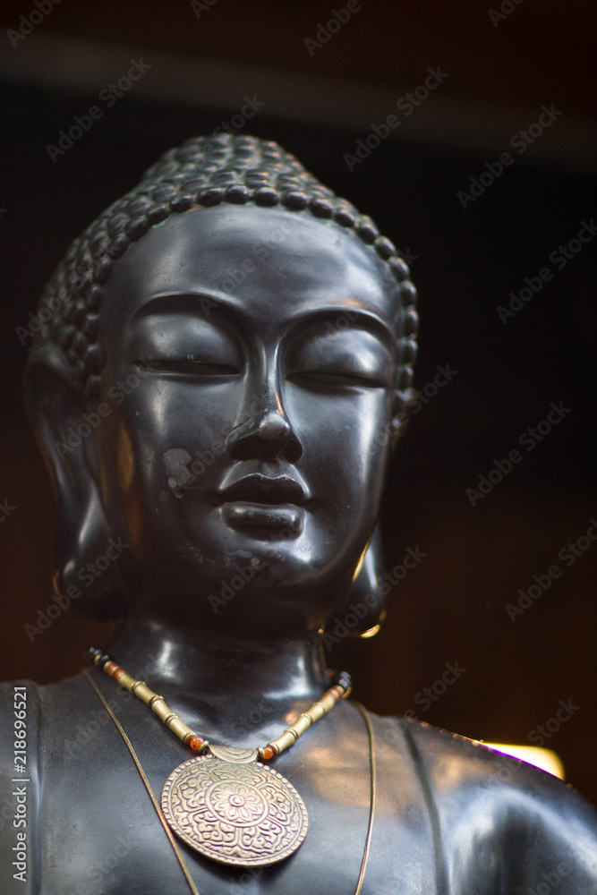 Black buddha statue made out of Ebony on a black background with a gold necklace